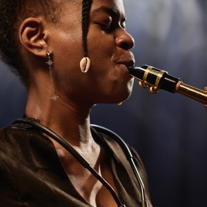 Side view closeup of young Black female musician playing saxophone on stage with focus on jewelry