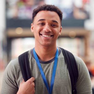 Portrait Of Smiling Male College Student In Busy Communal Campus Building